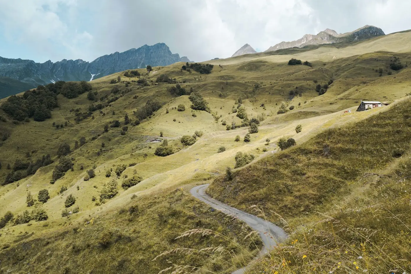 Image représentant une montagne en été avec des nuages et un chalet d'alpages sur le côté droit.