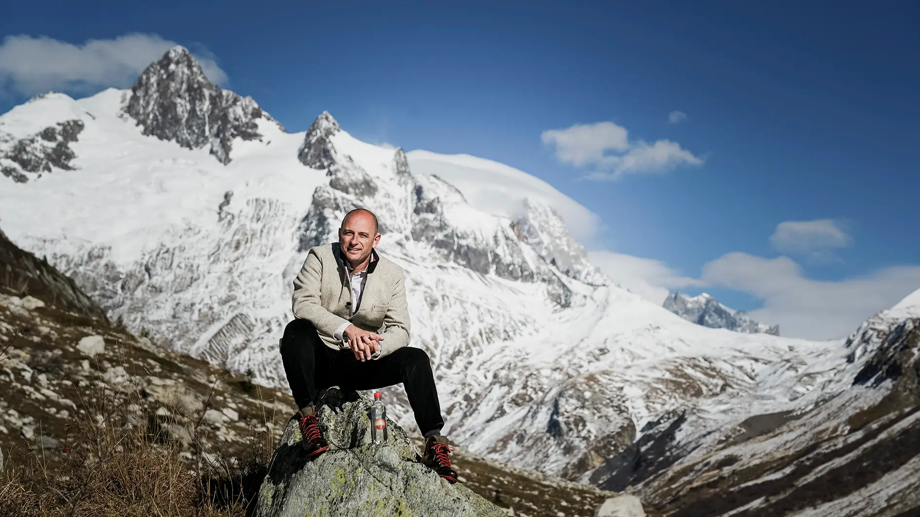 Visuel d'un homme assis sur un rocher devant une montagne