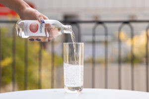 Main versant de l’eau gazeuse Bonneval dans un verre, sur une table en extérieur