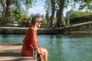 Femme assise sur un quai en bois au bord de l’eau avec une bouteille d’eau minérale naturelle Bonneval